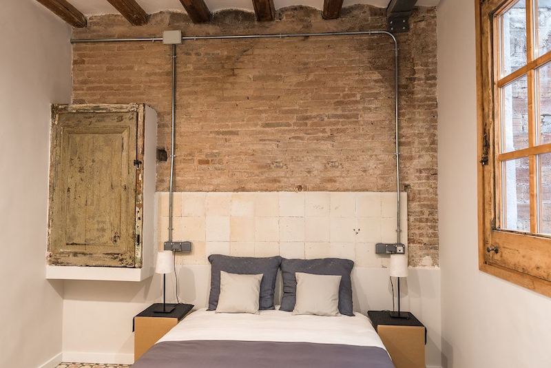 Apartamento con muebles de cartón y la instalación vista Dormitorio con cabecero de azulejos y mueble antiguo. Instalación de electricidad vista.