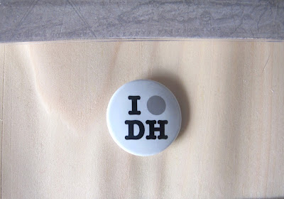 Badge saying 'I [spot] DH' on top of a sheet of wood veneer.