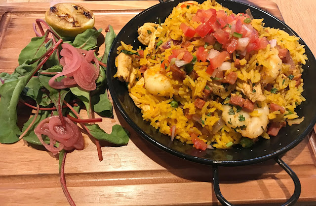 dish of cuban paella on a wooden board with side salad and lime