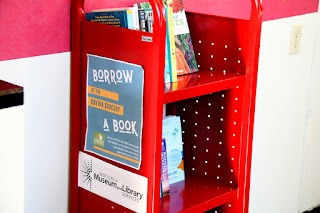 Books sit on a small red book cart. On the side it says borrow a book.