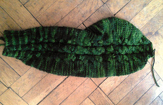 A sweater sleeve knit in the round.  It is laying flat on a wooden floor.  Three cables run down the sleeve. 