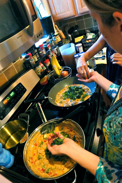 Two cooks in front of stove putting Thai Basil in Thai Red Curry Chicken prepared in two woks