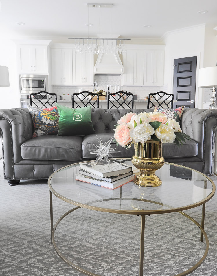 A glam and feminine living room with a gray chesterfield sofa, glass coffee table and a neutral rug by Karastan.