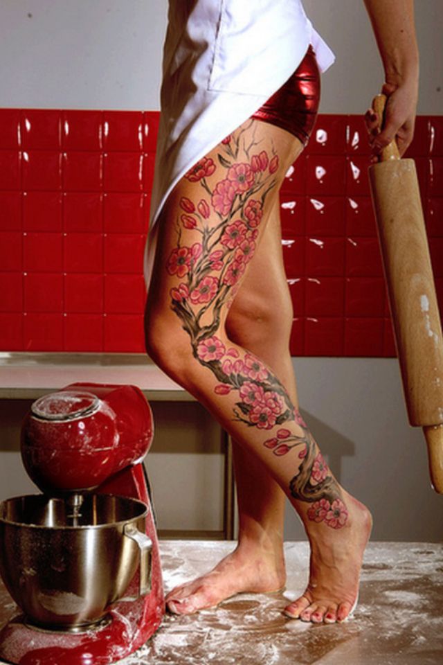 chica en cocina con bata, lleva la pierna tatuada con un arbol del cerezo