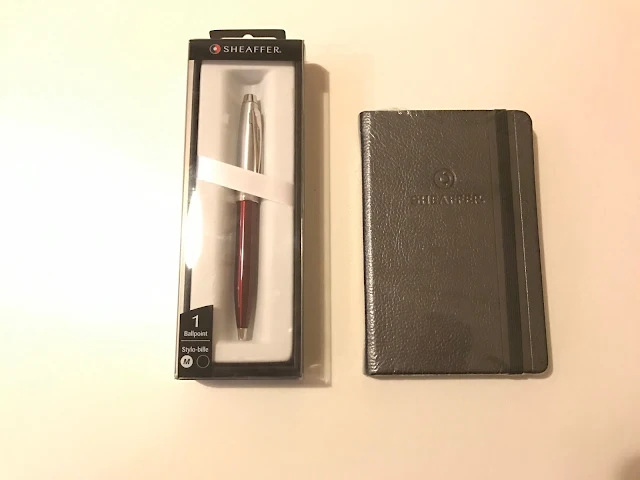 A Black Sheaffer notepad and a Ballpoint pen with a silvery top half and red bottom half in a display case