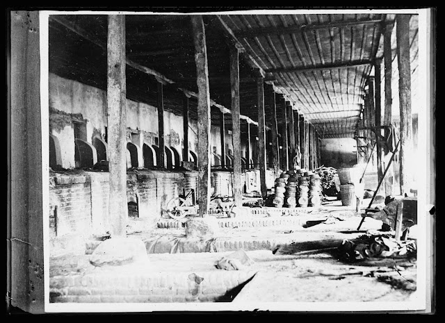 Part of the huge bakery at Monastir turned over to the A.R.C. by the French Army. If formerly supplied the Allied Army of the Orient with 125,000 loaves of bread a day. Now it is sued to help feed the starving civilian population in this district of the Balkans. The baskets heaped in the background are used to hold the kneaded dough, which is placed in the pits drawing heat from the fire-boxes, to rise. The fires are raked out and the dough is put into the fire-boxes on long planks being baked by the heat retained in the sontes. Each loaf baked here weighs three pounds and is in the shape of a fair-sized dish-pan. A mill where wheat is ground into flour adjoins the bakery and is operated by the A.R.C.