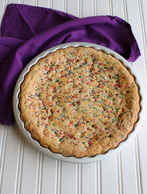 A supersized chewy vanilla cookie filled with plenty of festive sprinkles and white chocolate chips and topped with frosting and more sprinkles. This cookie cake is what birthday dreams are made of.