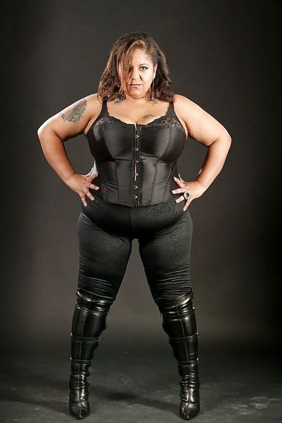 strong dominant woman with curves, dressed in black boots and bustier with her hands in her side.