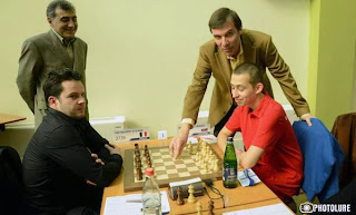 Ci-contre, le président bulgare de l'European Chess Union (ECU) Silvio Danailov joue le premier coup symbolique de la partie de la table 1 entre Petenyi et Bacrot, en présence du grand-maître arménien Smbat Lputian © site officiel