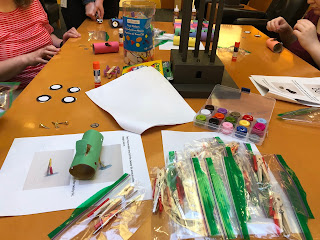 four sets of hands working with various art materials to create automobile craft at wood table