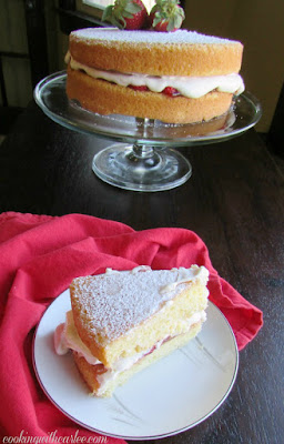 Two layers of sponge cake sandwich fresh whipped cream, strawberry jam and fresh strawberries. My take on a tea time classic treat. slice of victoria sponge cake with remaining cake on pedestal in background