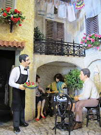 One-twelfth scale miniature scene of a European courtyard with a waiter serving diners.