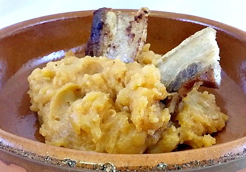 Un plato de barro con patatas con pimentón coronado con panceta