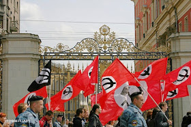 Marchers carrying flags with black hammer and sickle in a white circle on a red field