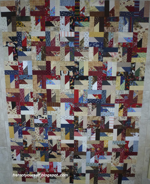 Straight set Puddin' and Pie quilt top Western fabrics in red, black, brown and blue alternating with white and tan fabrics create the windmill shape of the block.