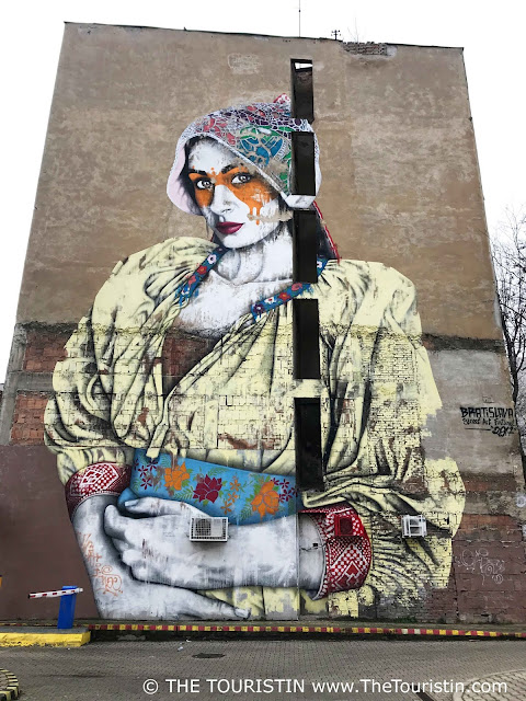 Mural of a woman in a yellow hoodie and blue and red coloured  cap on the facade of a house..