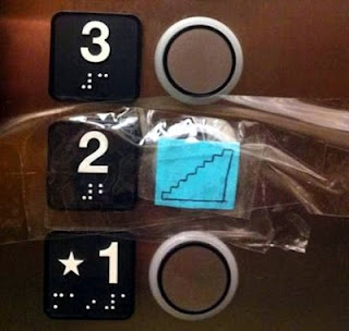 Elevator button panel with the second floor button covered with a drawing of stairs taped over the button, the raised number 2, and the Braille number)