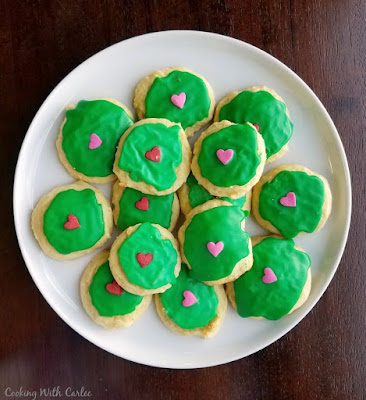 Sour cream cookies are simple, soft and oh so good. We fell in love at first bite so many years ago and they are still a favorite! sour cream cookies topped with green icing and a large heart sprinkle to mimic the Grinch