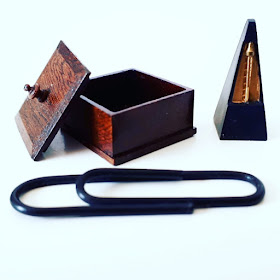 Full-sized paper clip with a one-twelfth scale miniature wooden box and a metronome next to it