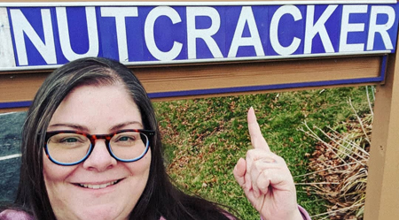 image of me standing underneath a sign that says NUTCRACKER, grinning and pointing upwards at it