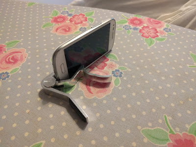 A phone held upright as it is clipped to a capo which is lying on its side.