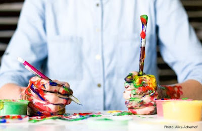 painted-smeared hand holding pen and paint brush