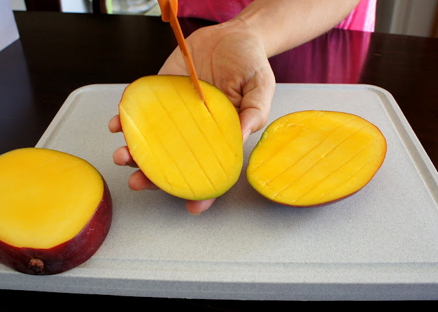 A hand cutting lines into a mango slice