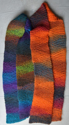 Two slip stitch scarves lying side-by-side; made from colour-changing yarn; left: blues, greens & dark greys; right: fiery oranges, reds and charcoal.