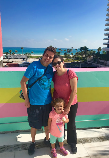A family of three pose for a photo on a colorful balcony with the beach in the background