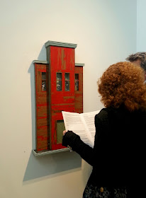 Two people looking at an exhibition catalogue in front of an Alex Asch piece hanging on the wall.