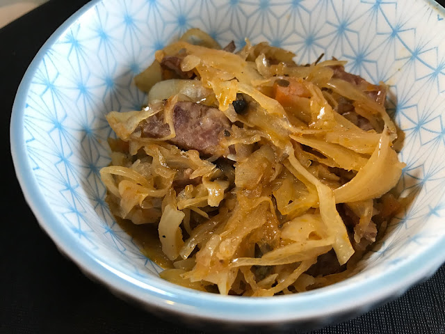 Bigo A small white bowl with a blue pattern with shredded cabbage, sausage and other ingredients which make up bigos