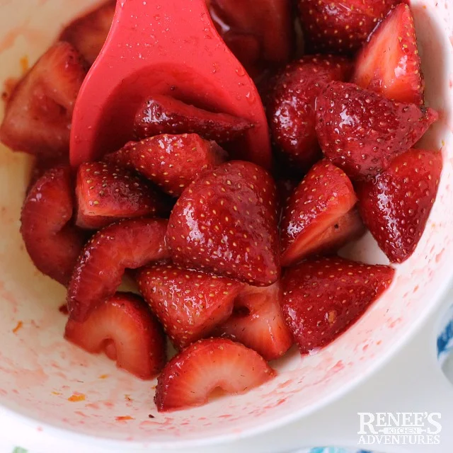 Sugar and orange zest mixed well with strawberries in a white bowl for Strawberries Romanoff | Renee's Kitchen Adventures