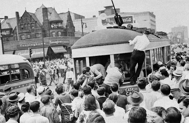 A woman passenger climbs out of the rear window of a tram in Detroit, Michigan, on June 21, 1943, after a mob halted the car in an effort to remove the black passengers on board during race riots.
