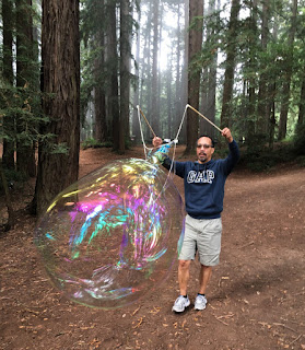 Front shot of a man producing a large, elongated soap bubble using sticks and string