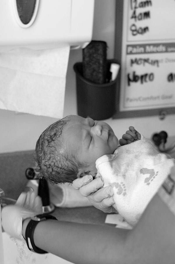 Black and white photo of a nurse washing swaddled newborn baby boy in sink after delivery.