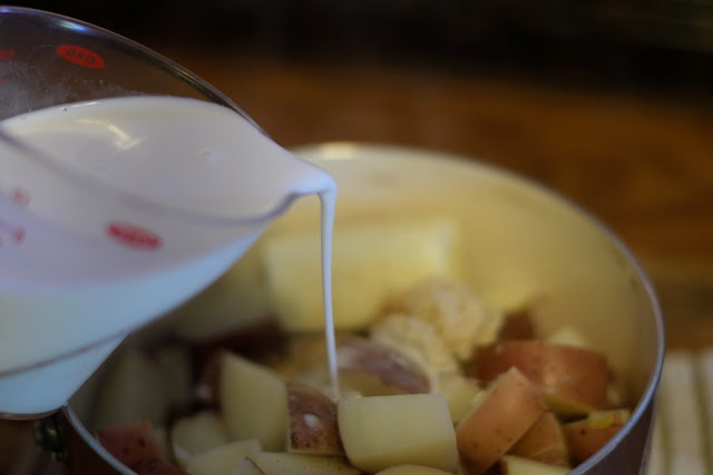 Cream being added to the pot of cooked red potatoes. 