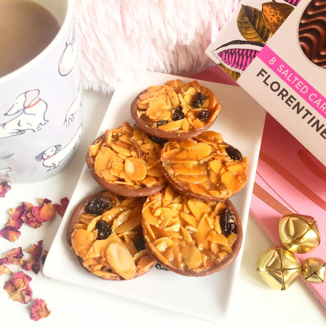 trinket dish in the centre with florentines on top. Cup of tea to the left, pink notebook underneath to the right with box of florentines on top