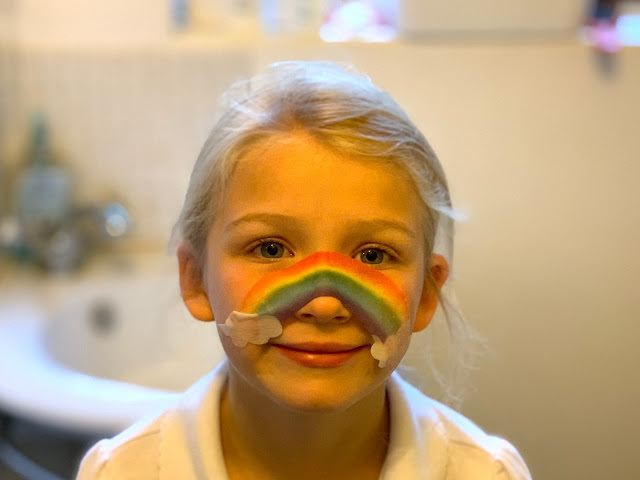 A young girl with a rainbow sheet facemask on her nose