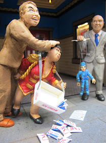 Three figures in front of a modern dolls' house miniature cinema lobby. One man is attacking an usherette, who is twisting his groin with her hand, the other is holding a marionette.