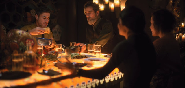 mesa decorada al estilo mexicano de la noche de los muertos, muchos vasos, platos, y bolsa con diferentes platos, imagen con todos anaranjados por la luz de las velas