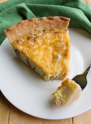 Enjoy a slice of ham, potato and cheese quiche any time of day, it's always good. Your whole family is sure to love it and you can customize it easily too! Slice of ham, potato and cheese quiche with first bite on fork