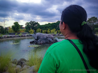 Woman Enjoy A Holiday Looking At The Sweet Garden Pond With Sleeping Bull Statue At Badung, Bali, Indonesia