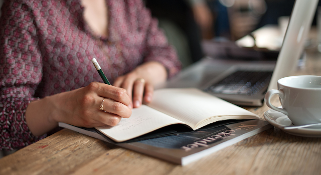 woman sits at a table and writes into a notebook