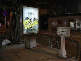 Advertisement sign for Elvis Costello concert next to a street sign for Estrada Da Areia Preta in Macau