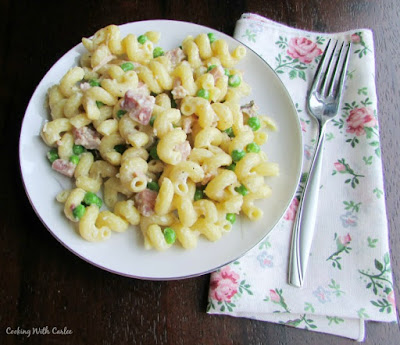 This all in one meal is a delicious combination of ham, pasta, peas and just enough creamy Parmesan cheese sauce. It is a great way to use leftover ham and is sure to have everyone asking for seconds! pate full of pasta with ham peas and cream with a fork and flowery napkin