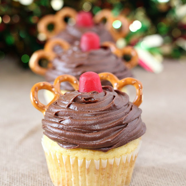 Super cute and easy to make, these Rudolph cupcakes are sure to make your day more festive! They are easy enough for the kids to hep make them and perfect for Christmas classroom parties as well. close up of a row of cupcakes decorated with chocolate frosting, a red gumdrop and pretzels to look like Rudolph