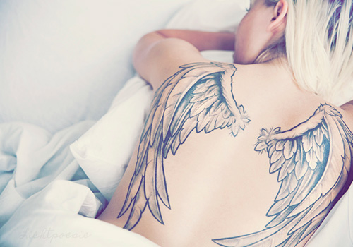 Modelo acostada boca abajo, duerme tranquila y vemos en su espalda el tatuaje de dos alas que le cubren la espalda