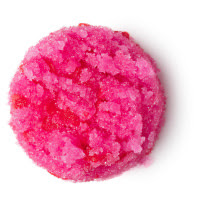 A pink solid circular lip scrub filled with little grains of sugar and salt topped with small red candy love hearts on a white background. 