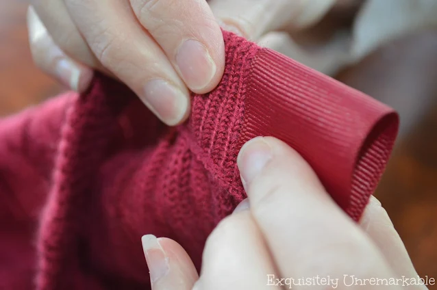 Fingers wrapping ribbon around frayed sweater ends