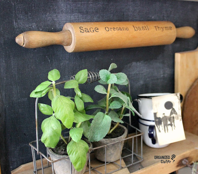 Photo of a herb name stenciled rolling pin hanging horizontally on a kitchen wall.